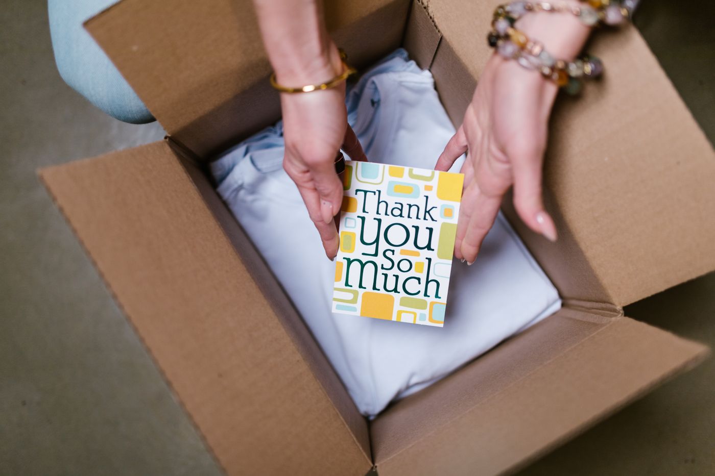 Hands opening a cardboard box with a thank-you card on top