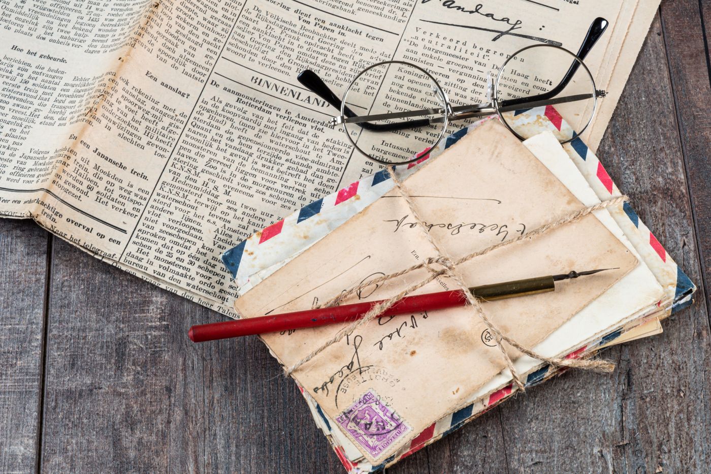 A bundle of old letters tied with string beside a pen and reading glasses
