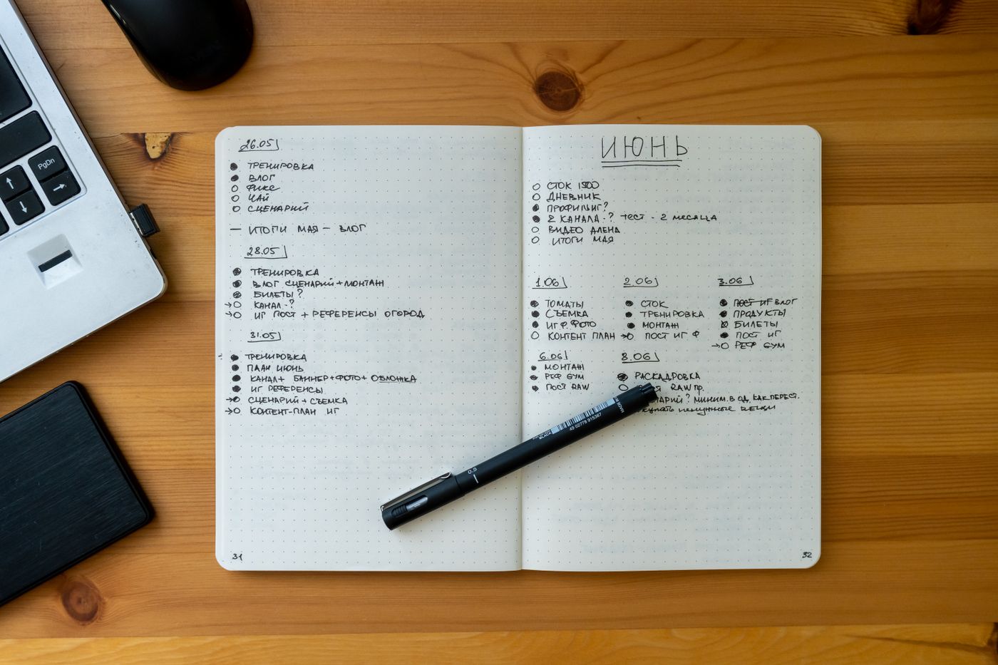An open notebook on a wooden desk with a handwritten list and a pen