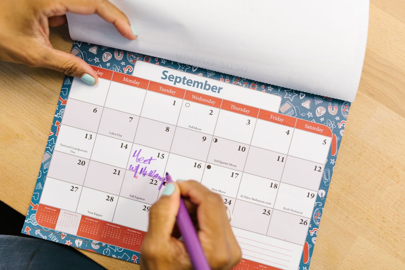 Hands marking dates on a paper wall calendar